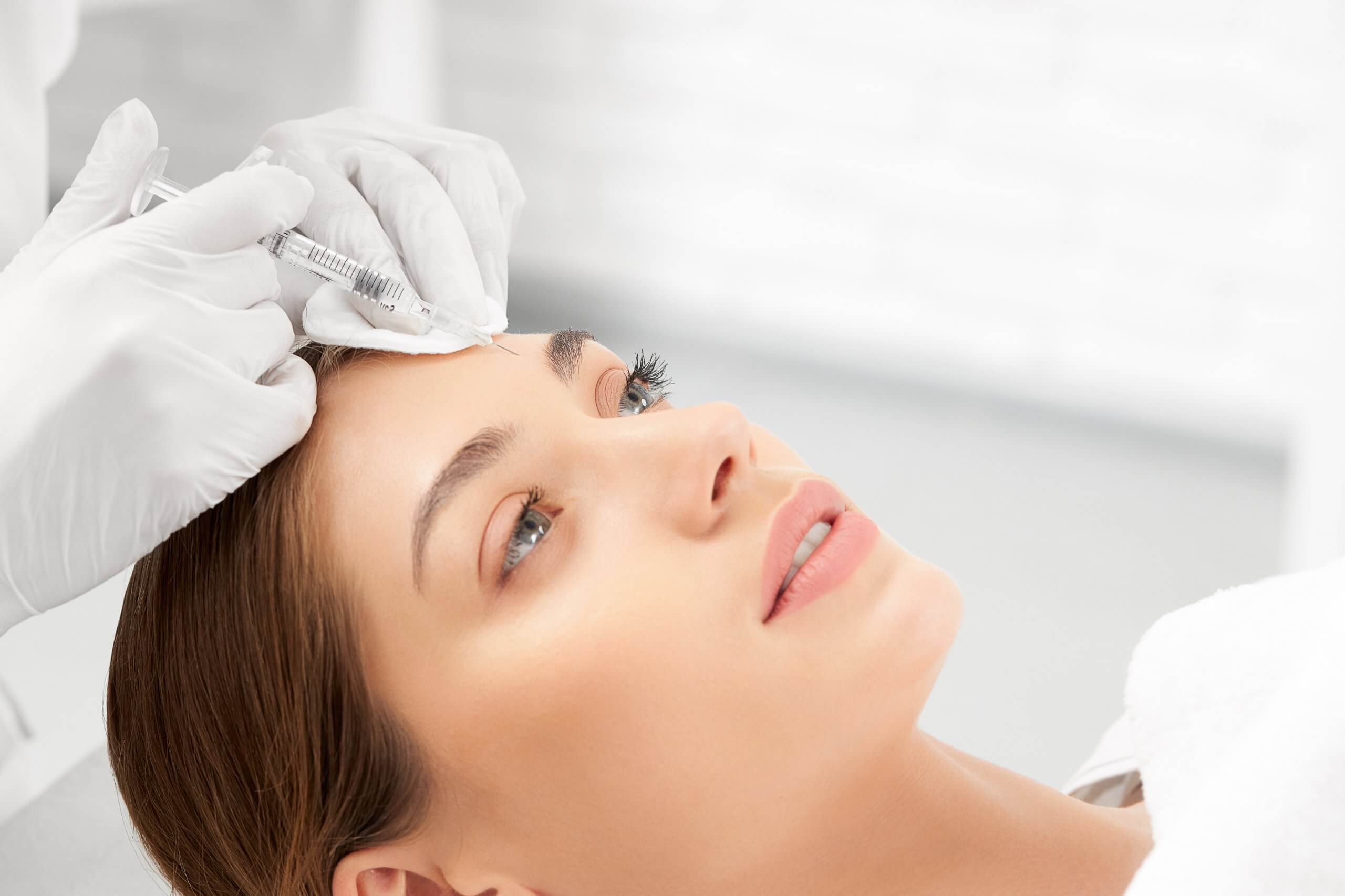 cosmetic nurse performs cosmetic injections on a client's forehead